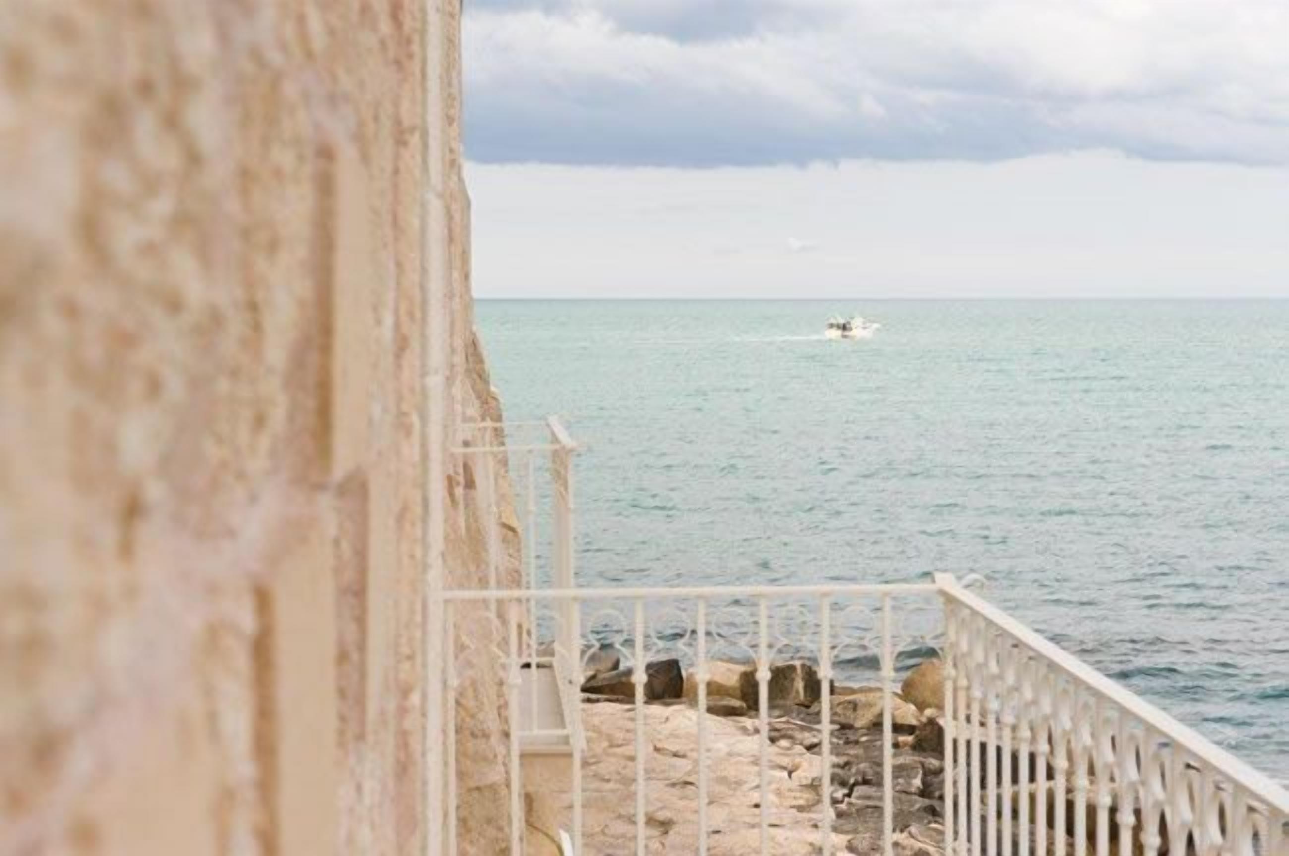 A stone building with a white railing overlooking a calm sea.
