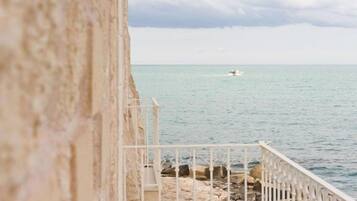 A stone building with a white railing overlooking a calm sea.