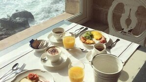 A breakfast table with plates of food, a jug of water, and a view of the ocean.