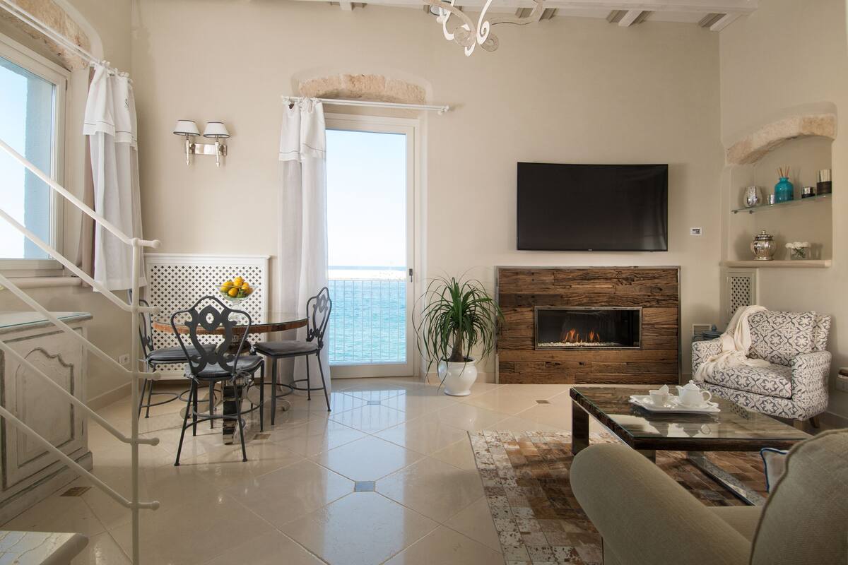 A spacious living room with a fireplace, a dining area with chairs and a table, and a balcony with a view.