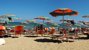 Uma praia com fileiras de espreguiçadeiras e guarda-sóis coloridos.