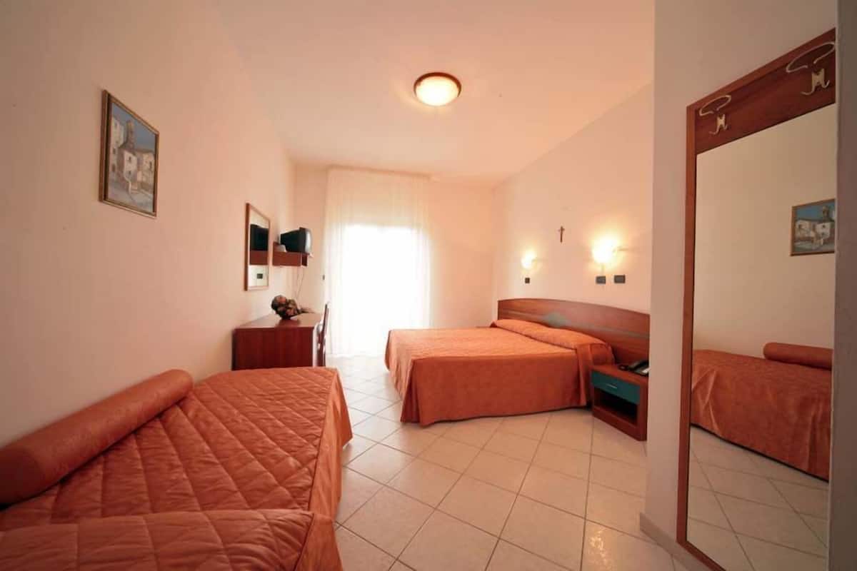 Ein Hotelzimmer mit zwei Betten, einem Schreibtisch, einem Stuhl, einem Spiegel und einem Fenster mit Vorhängen.
