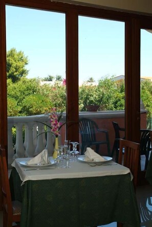 An outdoor dining area with a table set for two, a vase with flowers, and a view of greenery and buildings. - Hotel Residence Adria (Rodi Garganico)