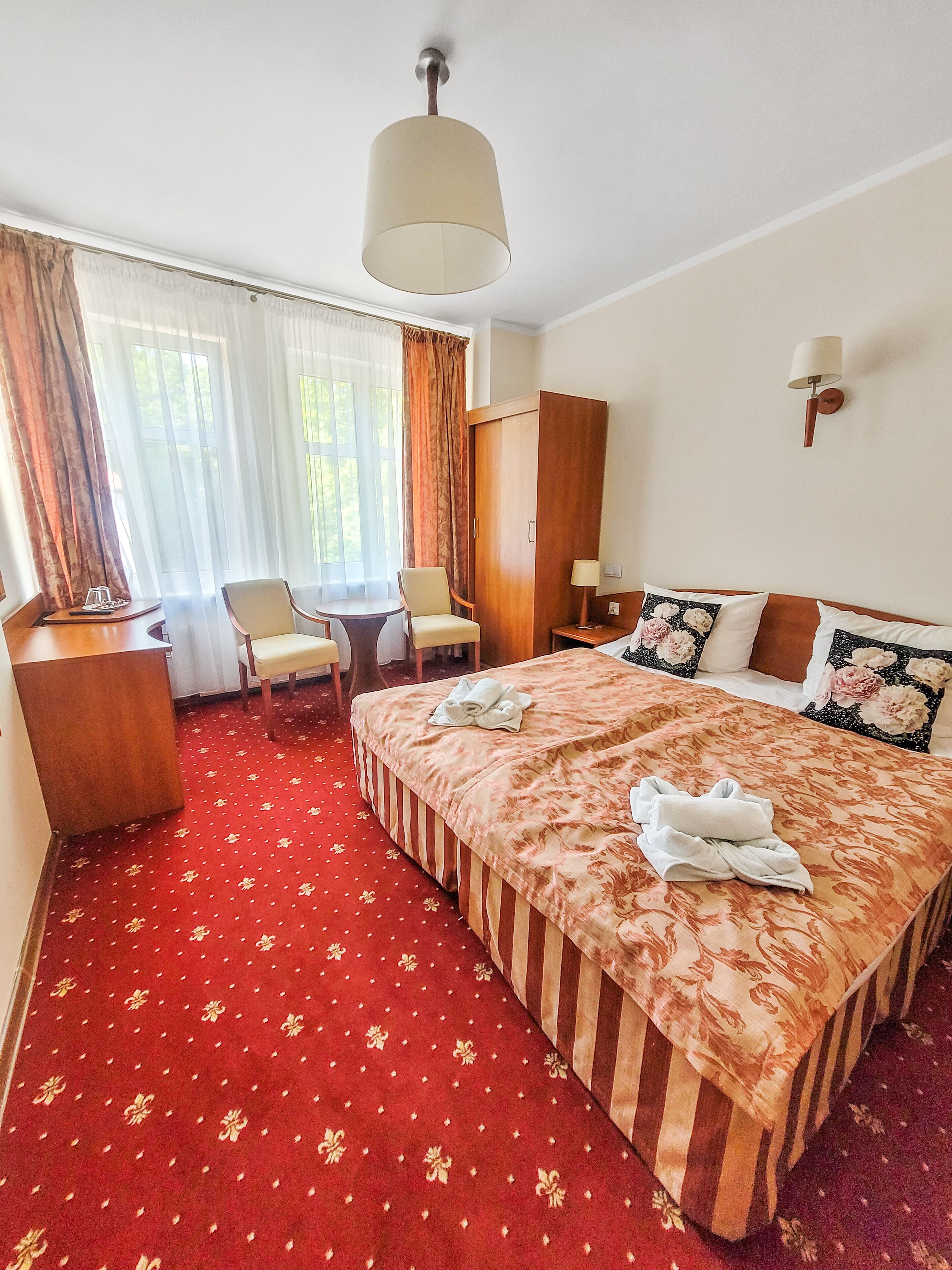 A hotel room with a bed, a desk, a chair, a lamp, and a window with curtains.