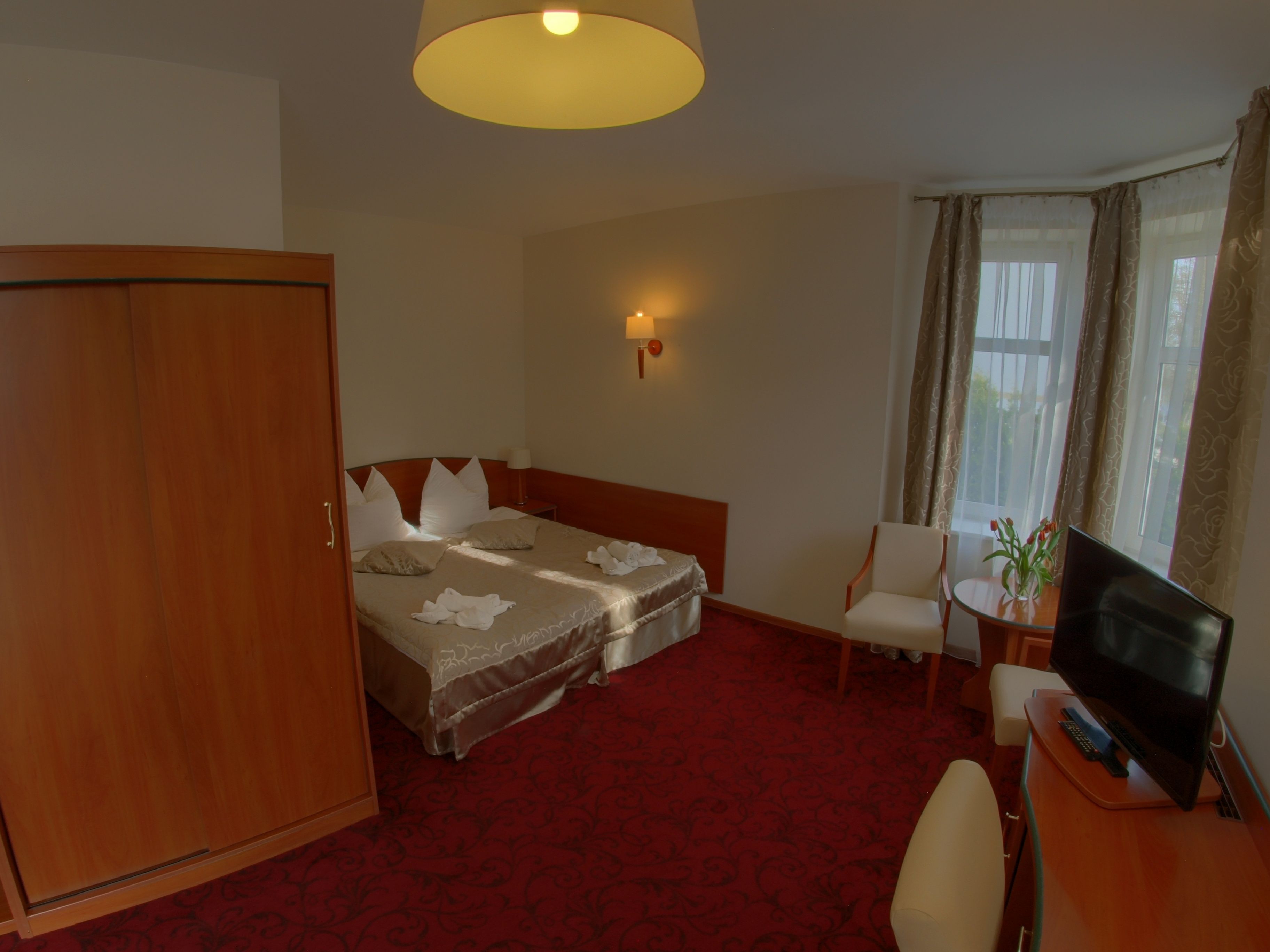 Habitación de hotel con cama, escritorio con computadora, silla, armario y ventana con cortinas.