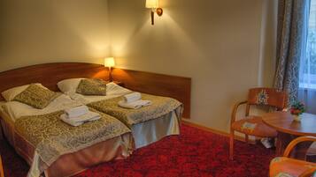 A hotel room with two beds, a red carpet, a wooden headboard, a small table with a chair, and a window with curtains.