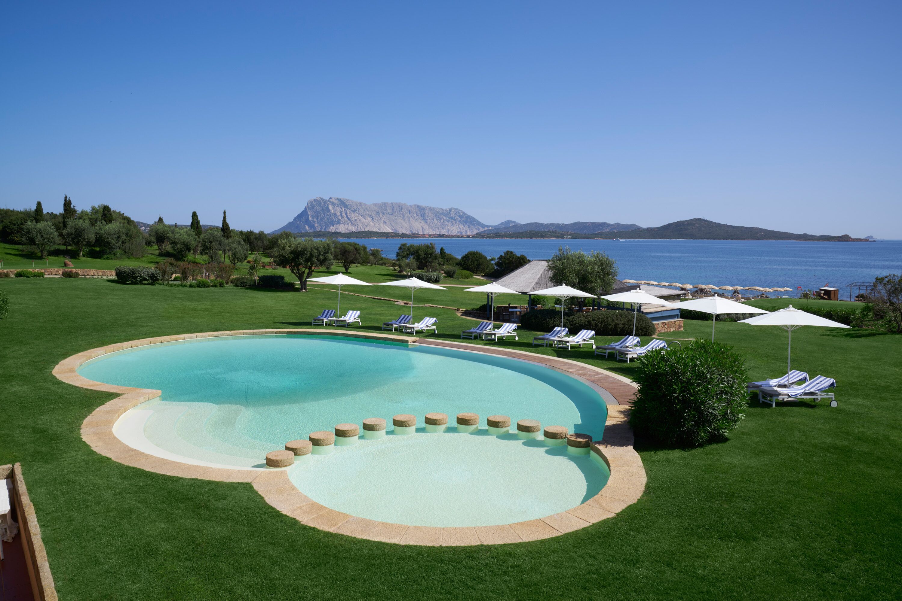 Une piscine entourée d’une terrasse, de chaises longues et de parasols.