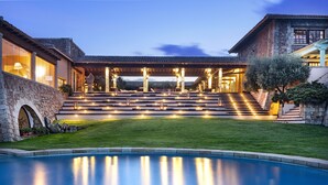 Une maison luxueuse dotée d’une piscine, d’une façade en pierre et d’un patio bien éclairé.