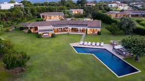 Une grande maison moderne avec une piscine, entourée d’une végétation luxuriante et avec des montagnes en toile de fond.