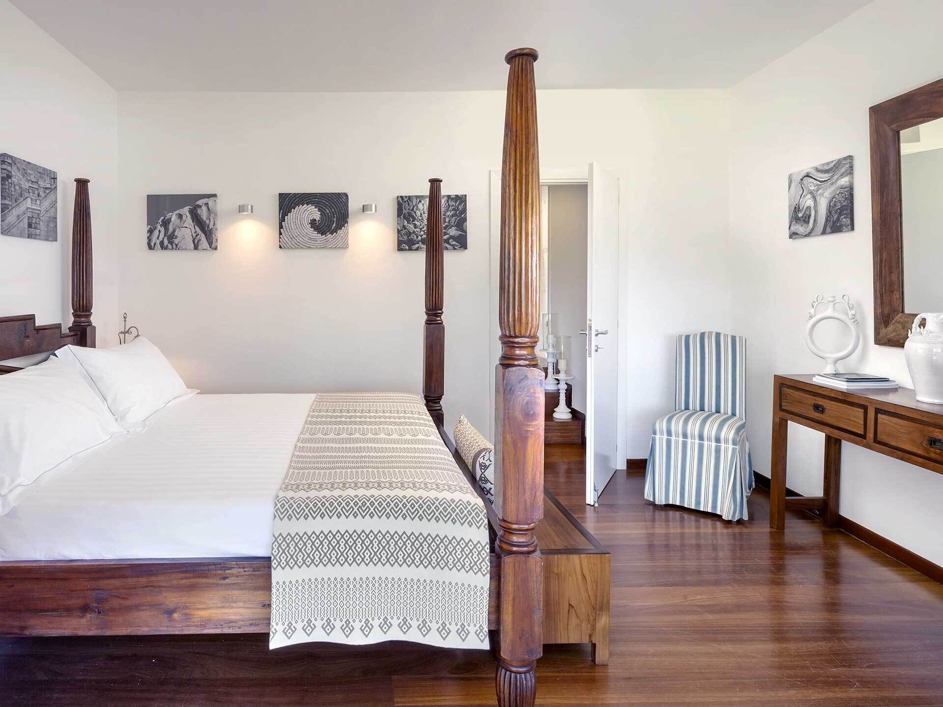 A bedroom with a four-poster bed, a wooden nightstand, a bedside table, and a chair.