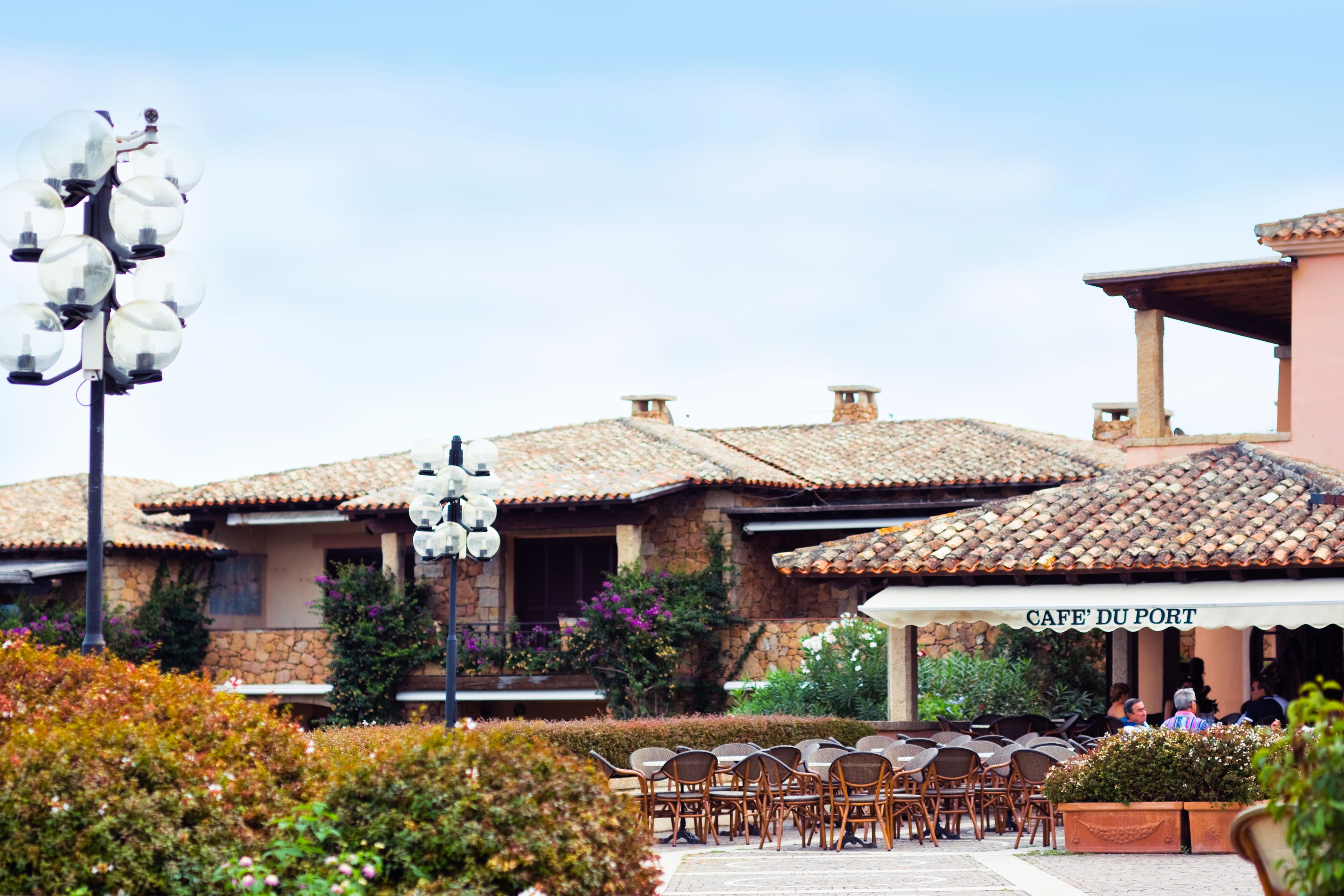 A cafe with outdoor seating, stone buildings, and a clear sky.