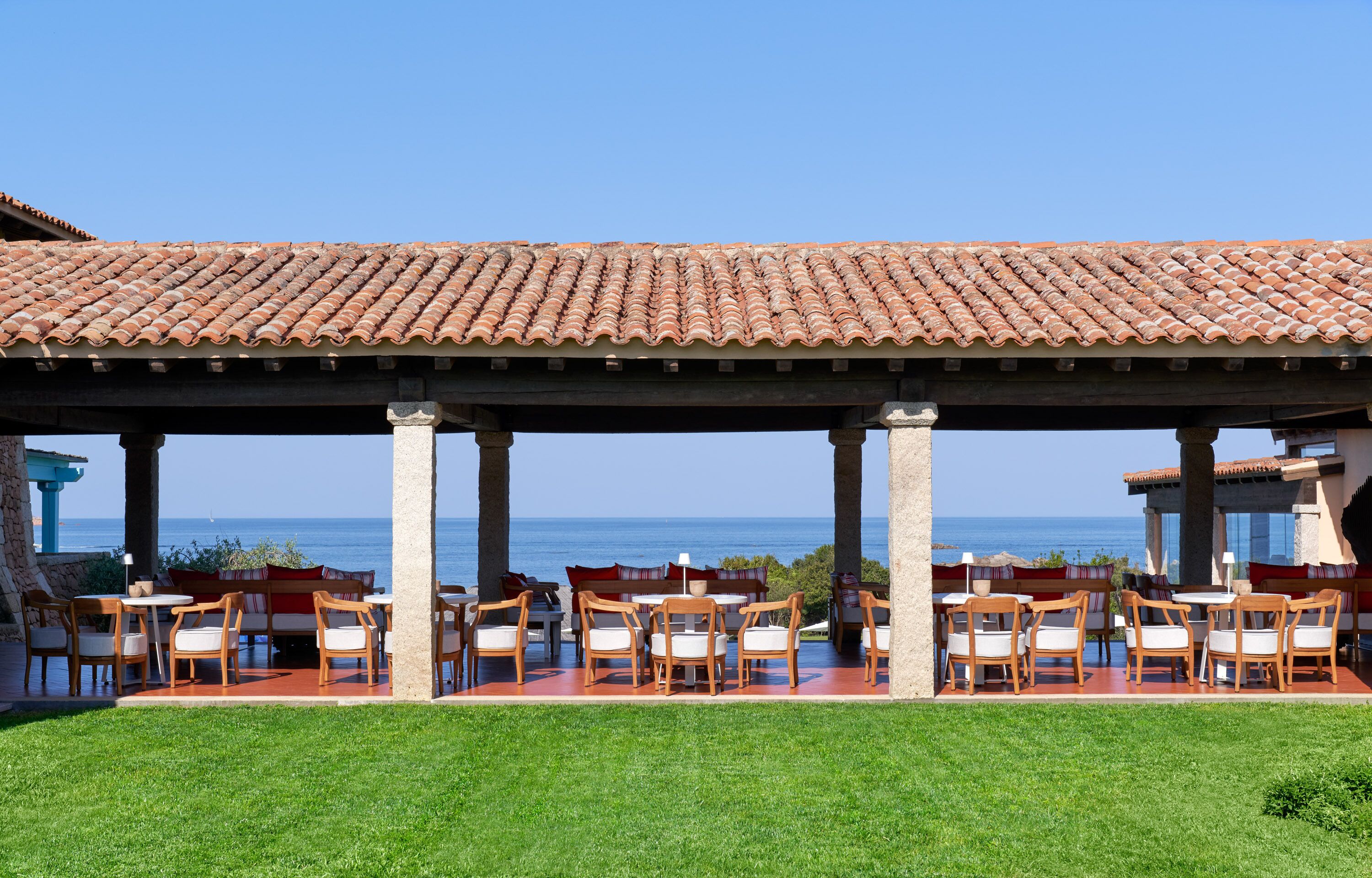 A covered outdoor seating area with tables and chairs, overlooking the sea.