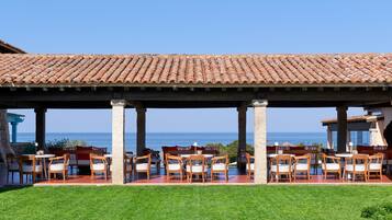 A covered outdoor seating area with tables and chairs, overlooking the sea.