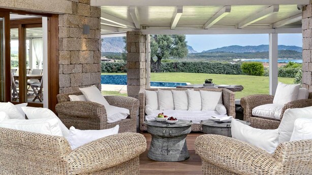 Un espace extérieur aménagé, abrité et doté de mobilier en osier, offrant une vue sur une piscine et des montagnes.