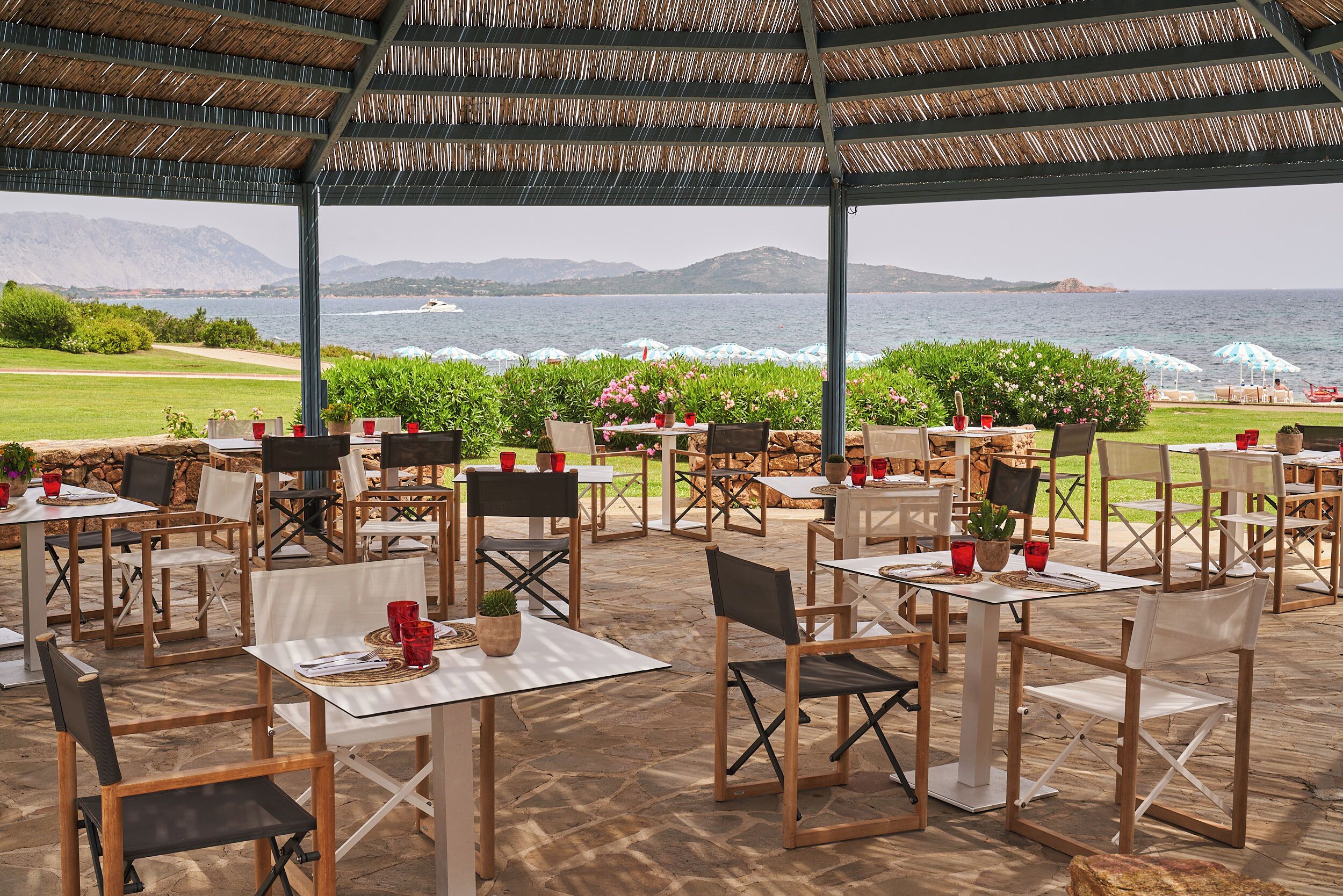 An outdoor dining area with tables and chairs, overlooking a body of water and mountains.