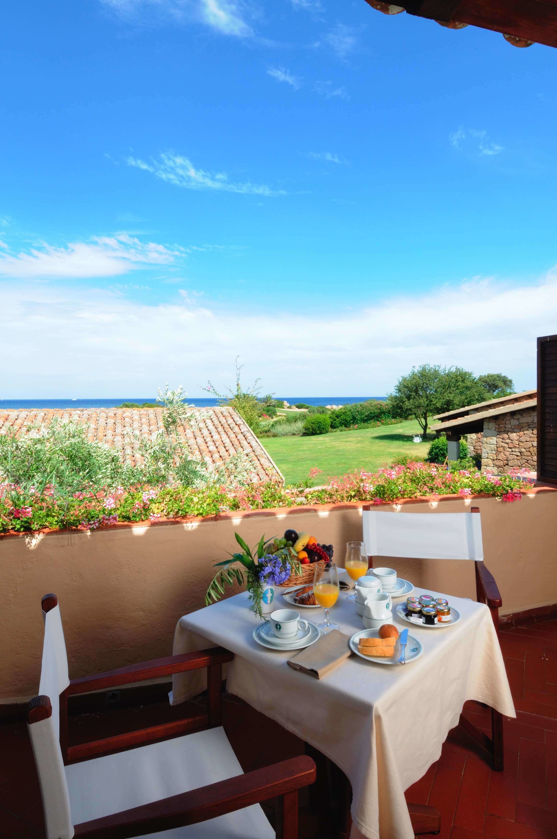 A table set with breakfast items on a balcony overlooking a golf course and ocean.