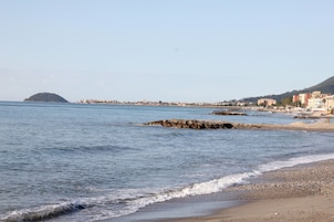 Vista costeira com praia, afloramentos rochosos e uma ilha distante.