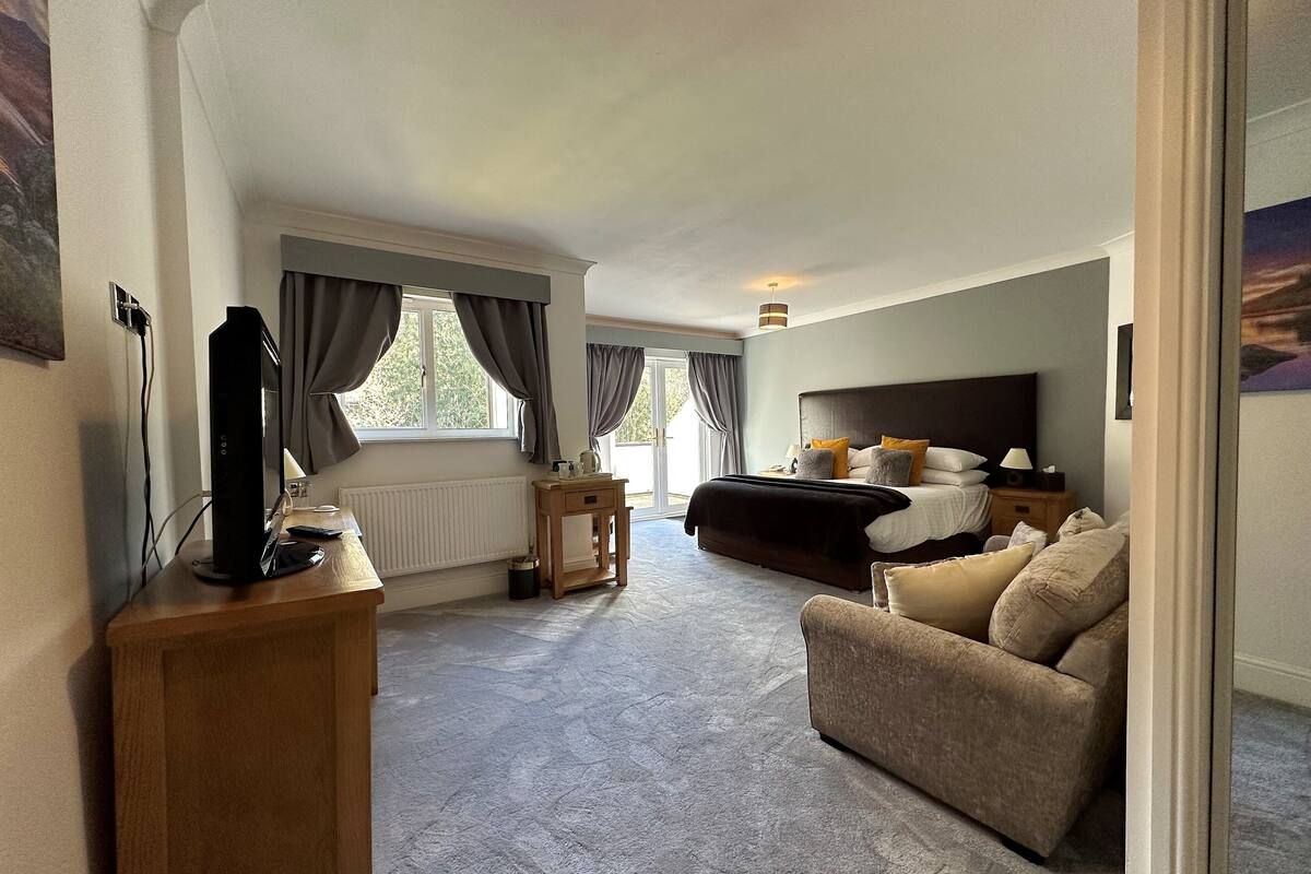 A bedroom with a bed, a sofa, a desk with a computer, and a window with curtains.
