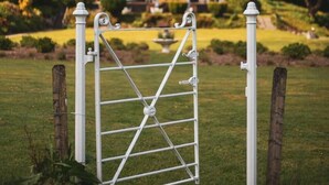A white metal gate in a grassy area with a house in the background. - Craig-y-Dderwen Riverside Hotel (Betws-Y-Coed)