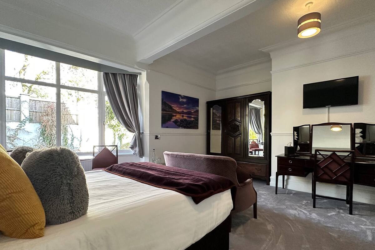 A hotel room with a large bed, a desk with a mirror, a TV, and a view of the outdoors.