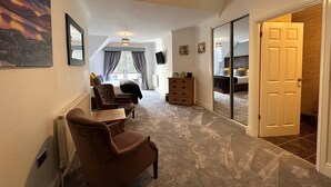 A spacious room with a large bed, a desk, and a chair. There is a sliding glass door leading to another room. - Craig-y-Dderwen Riverside Hotel (Betws-Y-Coed)