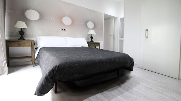 Un dormitorio moderno con una cama grande, dos mesitas de noche con lámparas, un armario y un diseño decorativo en la pared.