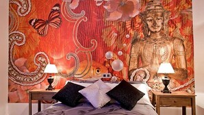 Un dormitorio con un gran tapiz que muestra a Buda, dos mesitas de noche con lámparas y almohadones decorativos.