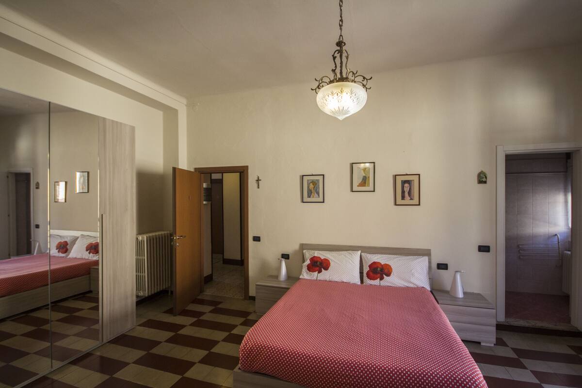 A hotel room with a checkered floor, a bed with red and white bedding, a chandelier, and a door leading to another room.