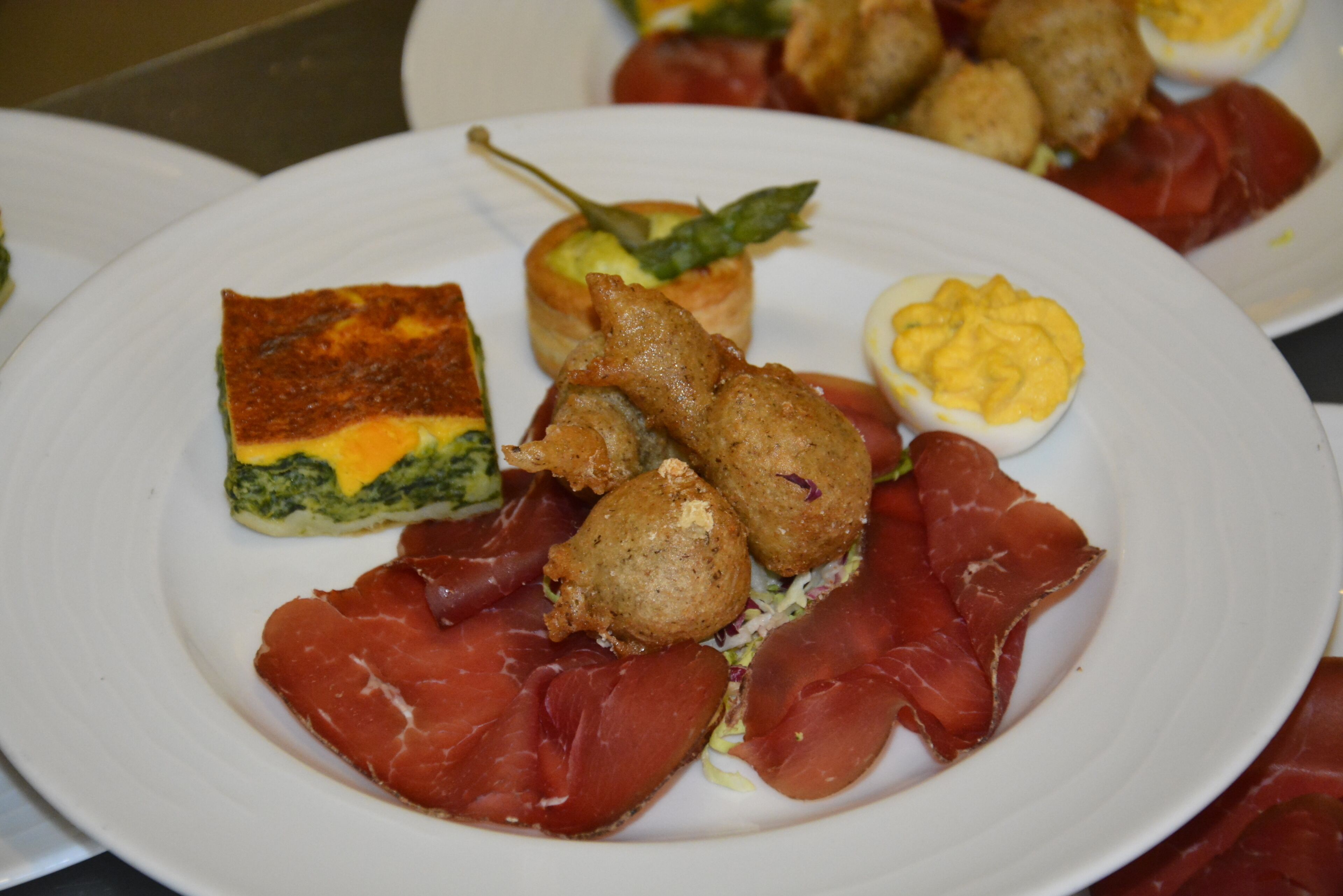 Un plato con diversos alimentos, como un trozo de carne, un huevo cocido y un pastel.