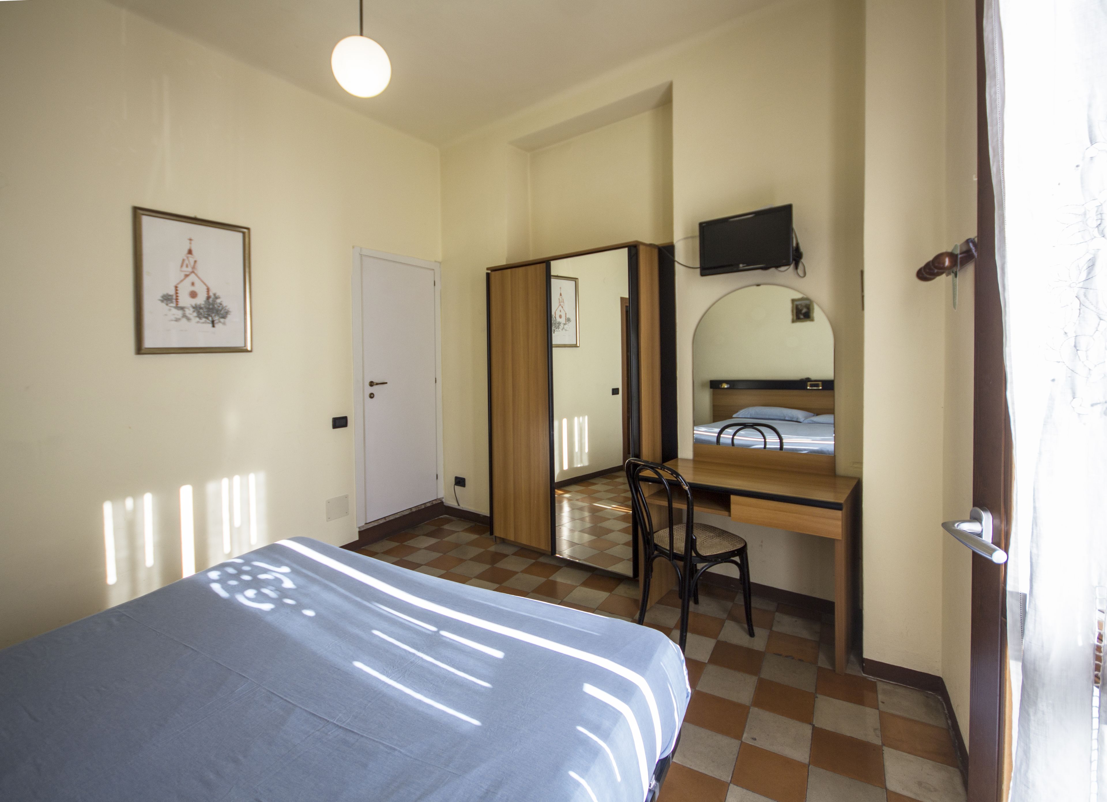 Ein Schlafzimmer mit einem Bett, einem Schreibtisch, einem Sessel, einem Fernseher und einer Tür.