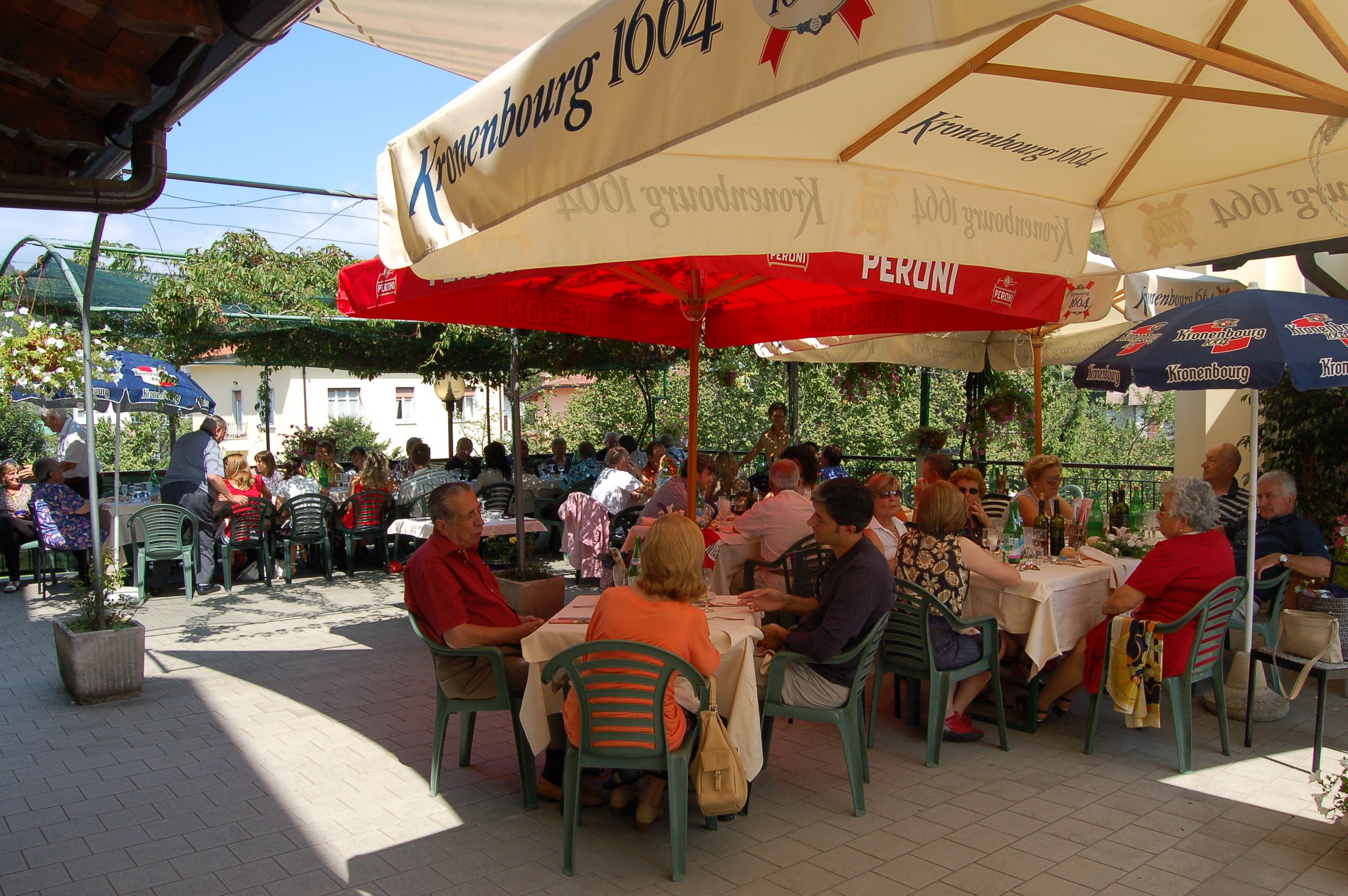 Een terras met tafels en stoelen onder parasols, omgeven door groen.