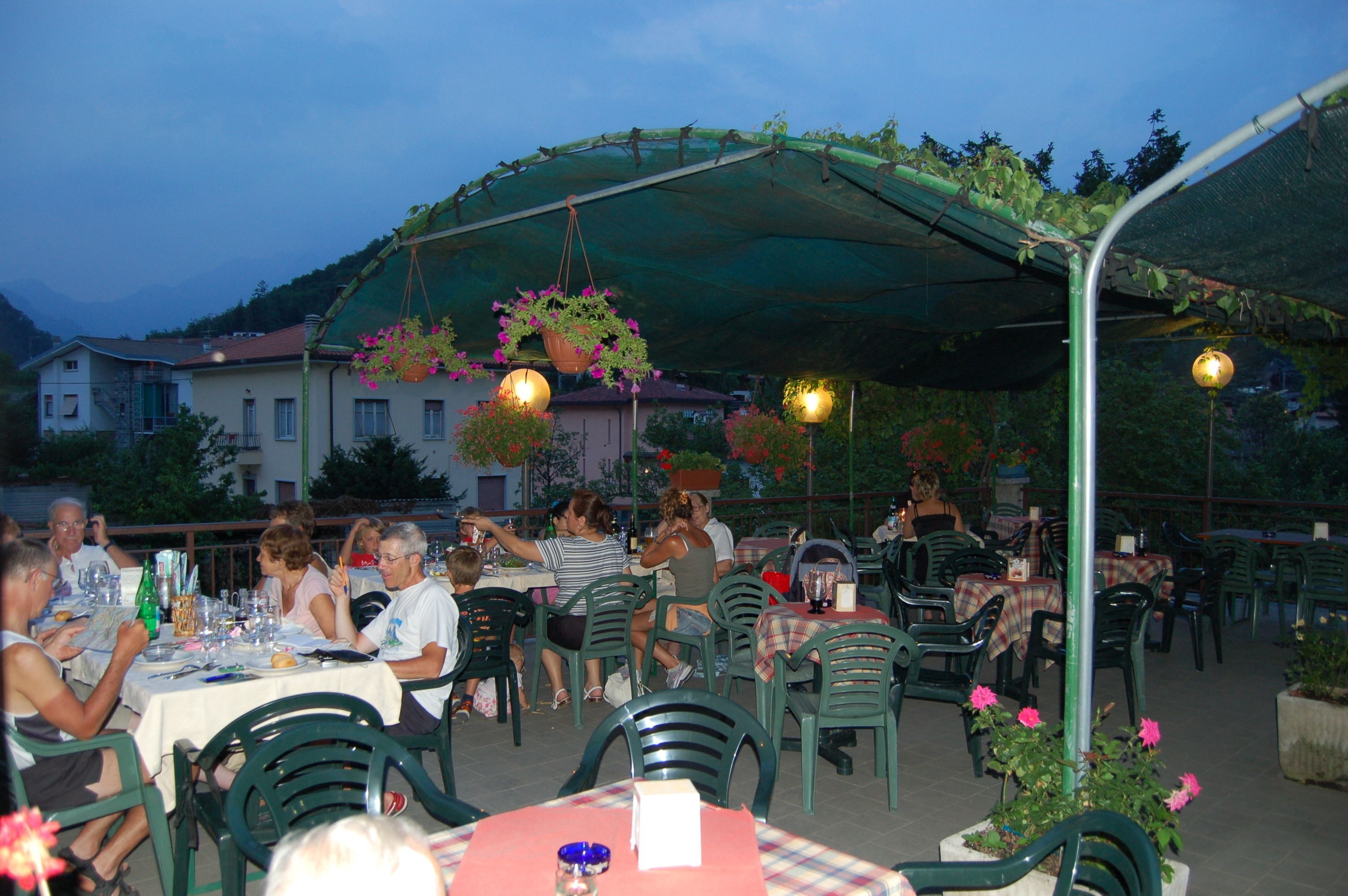 Un espace de restauration en plein air, avec des tables et des chaises, abrité par une pergola verdoyante et entouré d’immeubles.