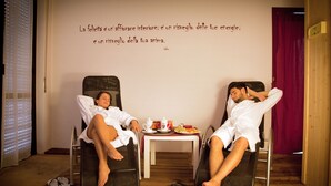 Two people relaxing in reclining chairs with a table between them containing a plate of fruit and a cup. - Albergo Sala (Valbrona)