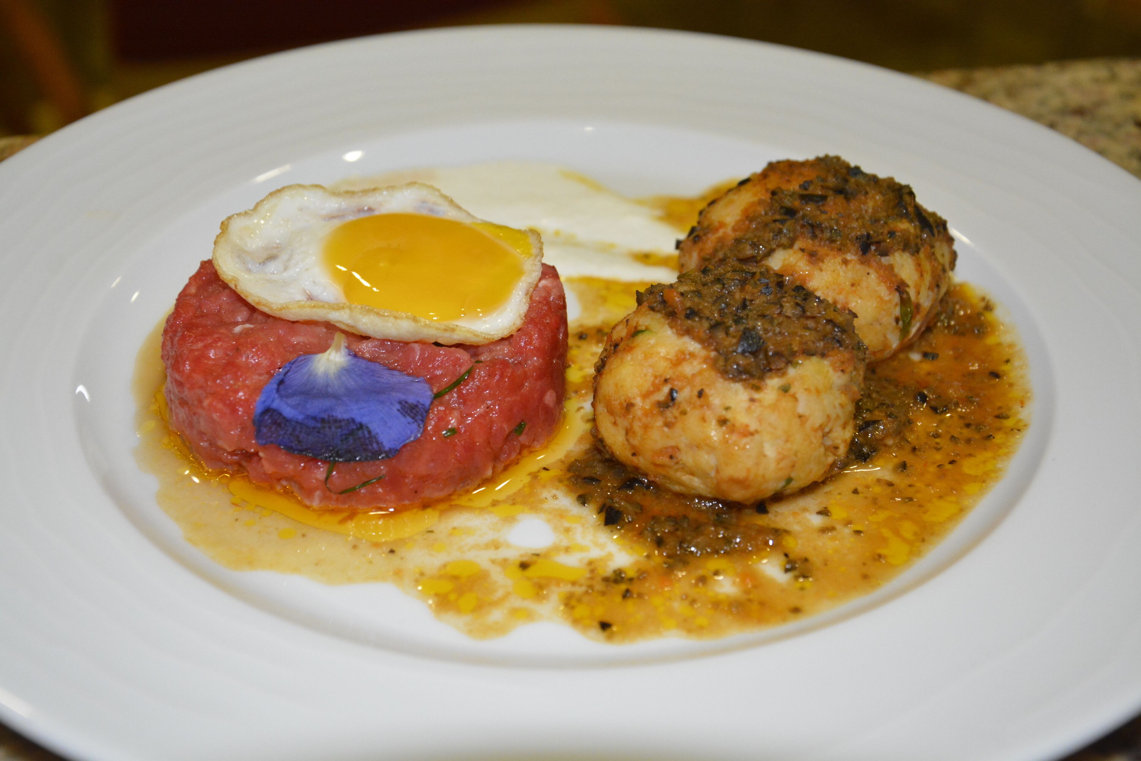 A plate with a steak topped with a fried egg and a piece of meat with a sauce.
