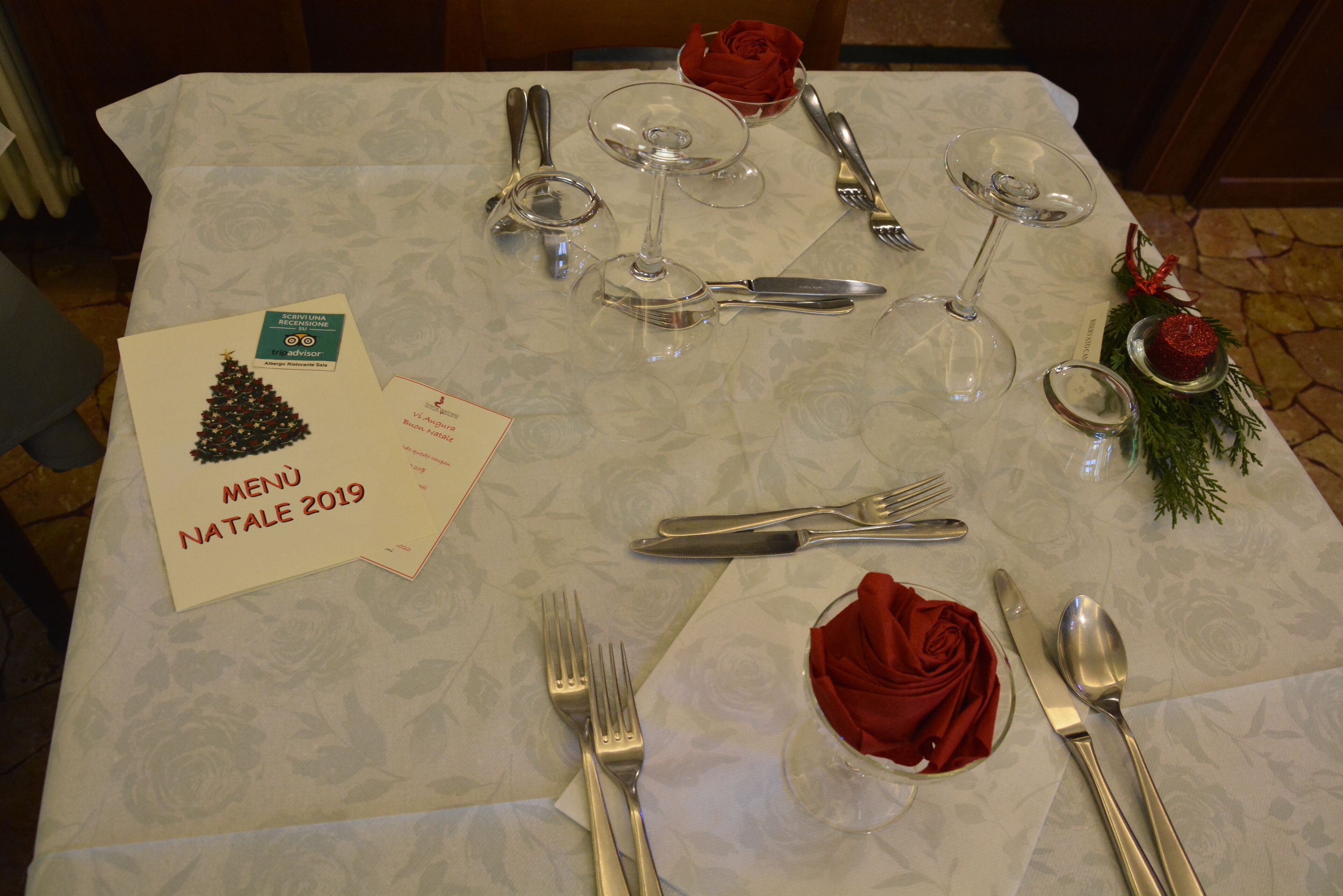 Una mesa servida para una comida, con un menú, cubiertos y una rosa decorativa.