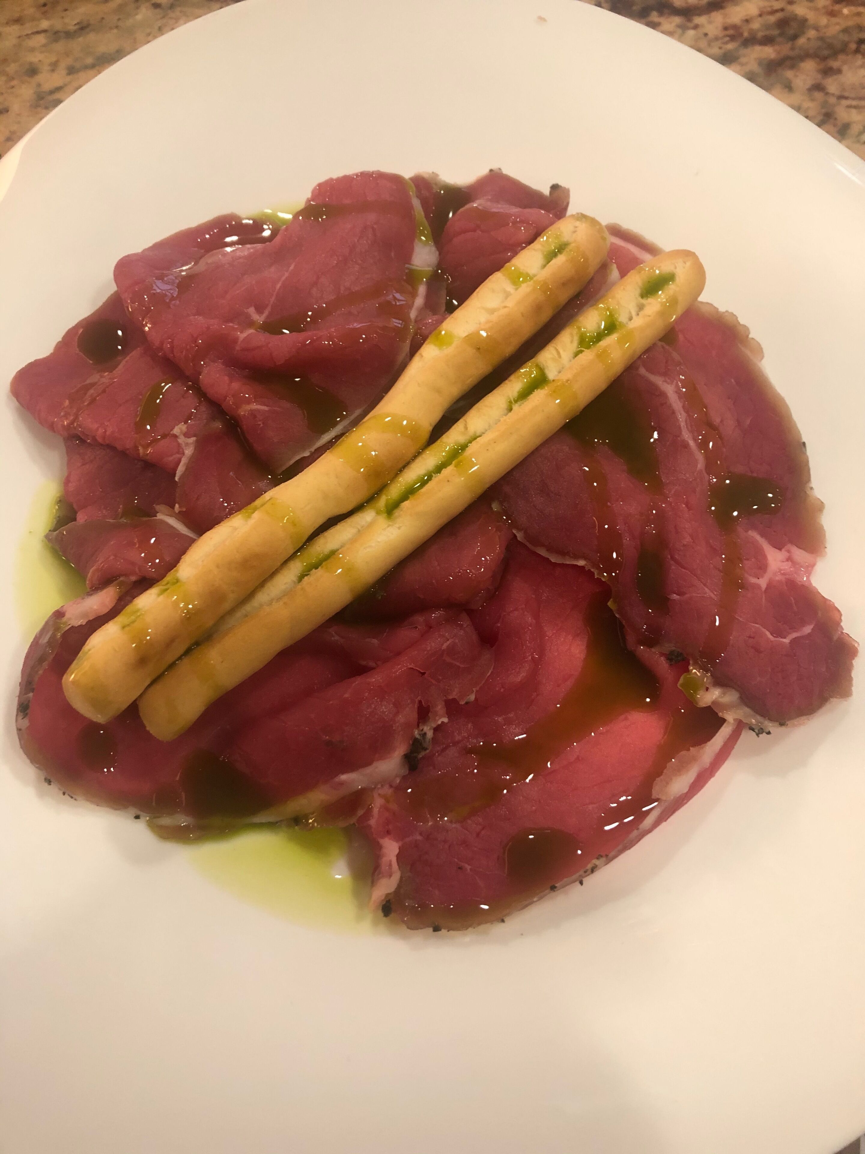 Un plato de láminas de carne cruda, adornadas con hierbas verdes y un palillo de madera.