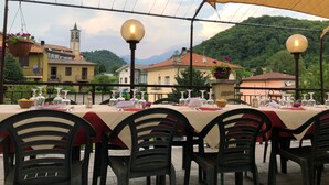 A terrace with tables set for dining, outdoor lighting, and a view of buildings and hills in the background. - Albergo Sala (Valbrona)
