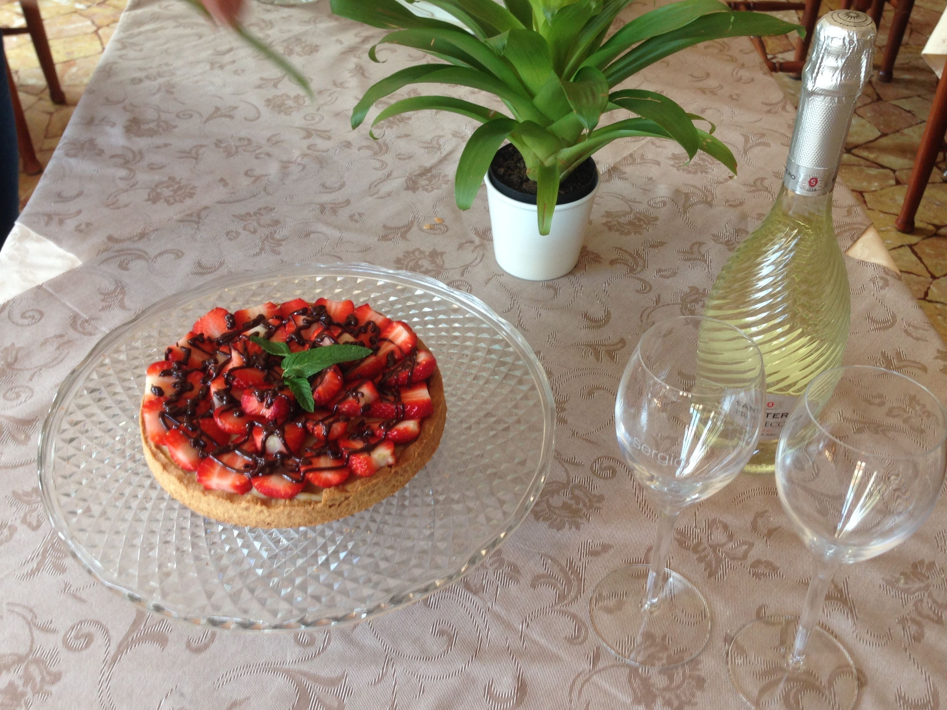 Een dessert op een glazen bord, een potplant en een fles wijn op een tafel.