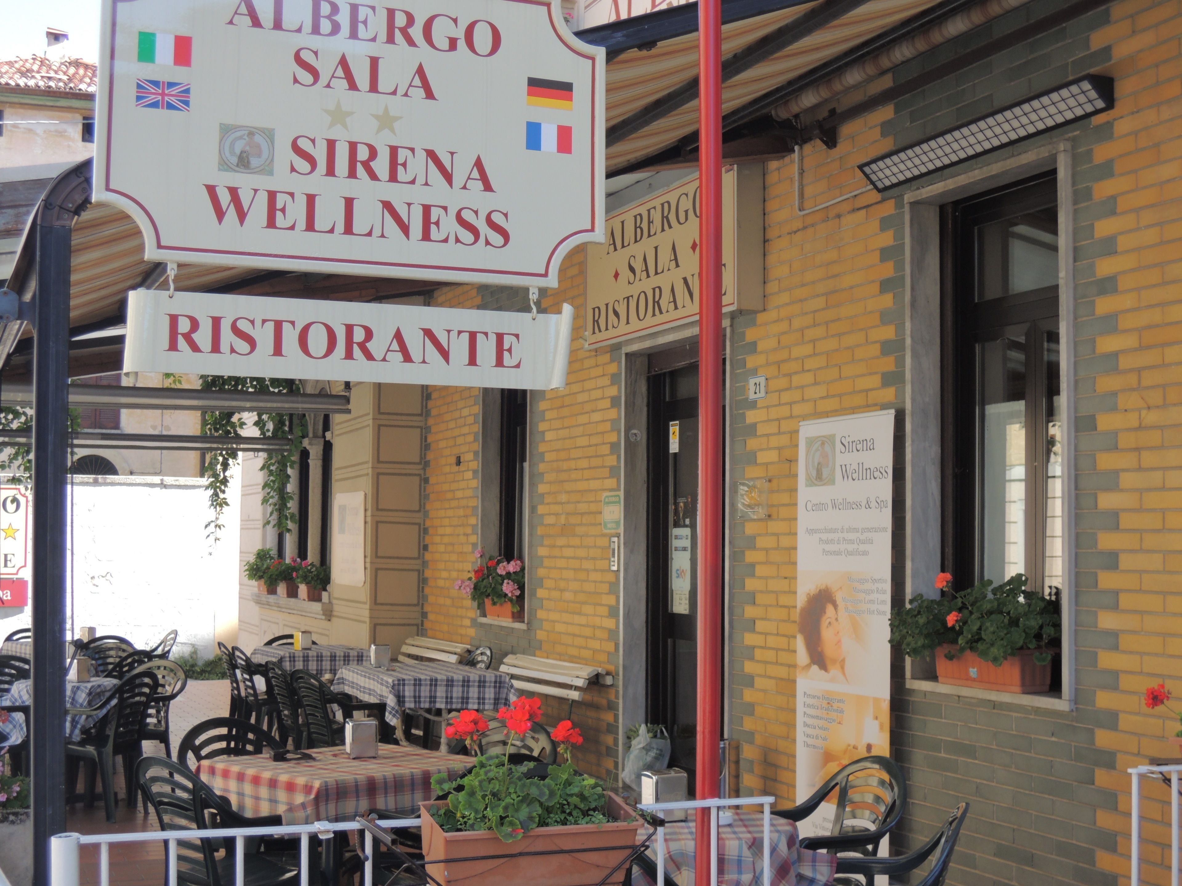 Ein Außenbereich mit Tischen und Stühlen, ein Schild für Albergosala Sirena Wellness und eine Ziegelhausfassade.