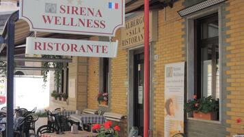 Ein Außenbereich mit Tischen und Stühlen, ein Schild für Albergosala Sirena Wellness und eine Ziegelhausfassade.