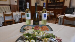 A dining table with seafood dishes, two bottles of wine, and a plate of oysters garnished with lemon and herbs. - Albergo Sala (Valbrona)