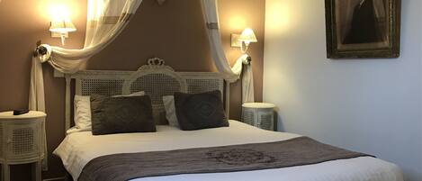 A bedroom with a four-poster bed, two bedside tables, a canopy, and a framed portrait on the wall.