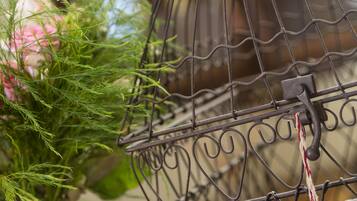 A metal birdcage with a handle, a pink rose, and a glass vase with green foliage.