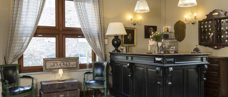 Una habitación con un ventanal grande, un armario de madera, una silla verde, una mesita con una lámpara y una lámpara de pared.