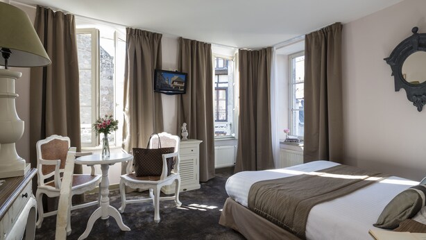 Quarto de hotel com cama, escrivaninha, cadeira e televisão.