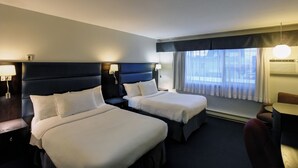 Una habitación de hotel con dos camas, un escritorio, una silla, una lámpara y un ventanal con cortinas.