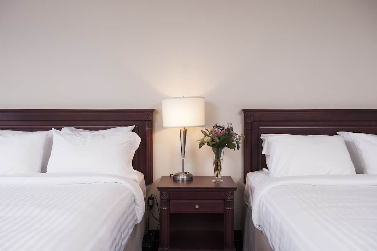 Una habitación de hotel con dos camas, una mesita de noche con lámpara y un jarrón con flores.