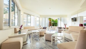 A spacious living area with a sofa set, a coffee table, and a TV mounted on the wall. - Dimitrios Beach Hotel Adults Friendly 14 plus (Rethymno)
