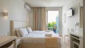 A hotel room with a large bed, a desk, a chair, a TV, and a balcony with plants. - Dimitrios Beach Hotel Adults Friendly 14 plus (Rethymno)