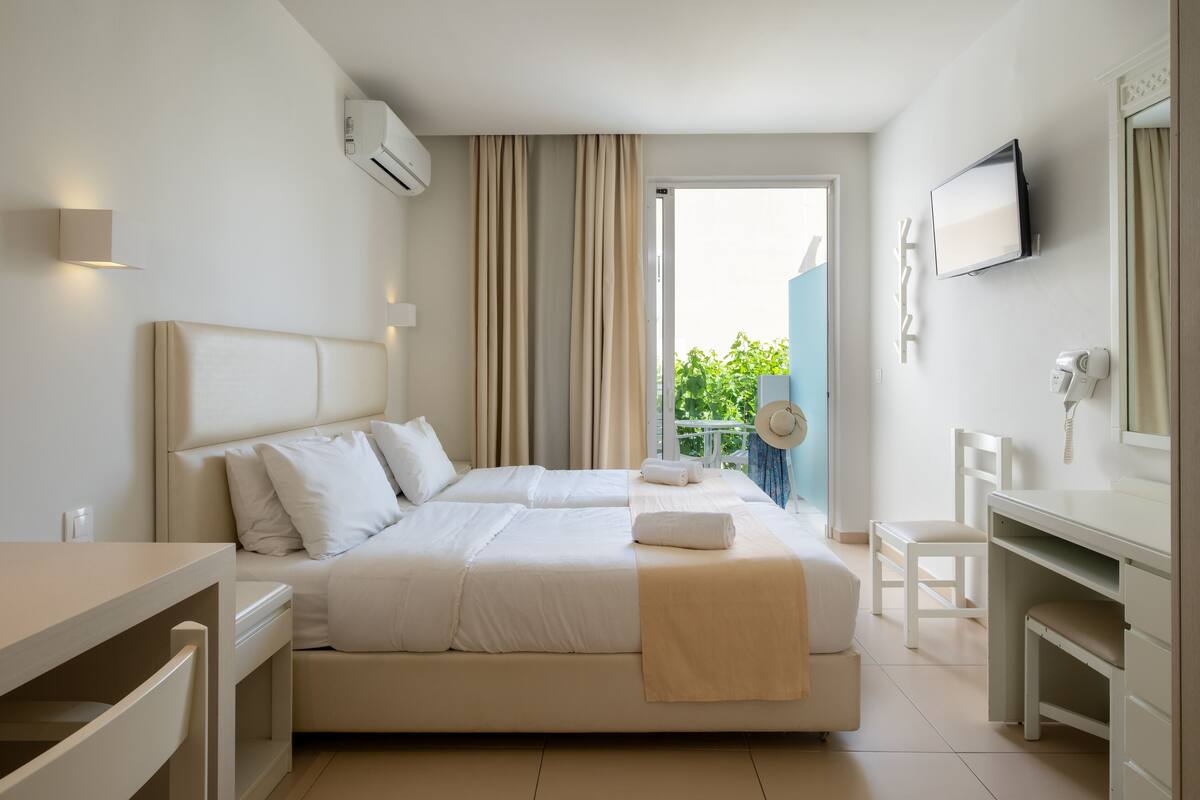 Une chambre d’hôtel avec un grand lit, un bureau, une chaise, une télévision et un balcon agrémenté de plantes.
